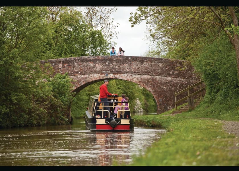 A Napton narrowboat cruising beneath a brick canal bridge.