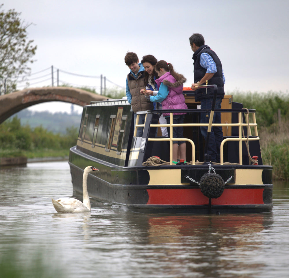 A family beside an Elite narrowboat, with a swan in the canal foreground