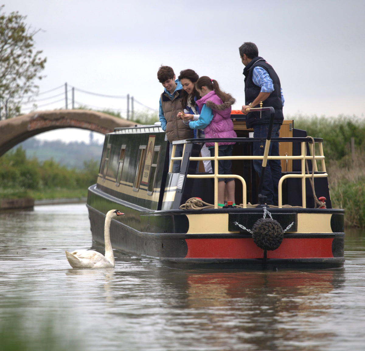 A family beside an Elite narrowboat, with a swan in the canal foreground